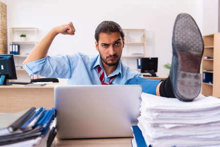 Young male employee unhappy with excessive work in the officeの写真素材