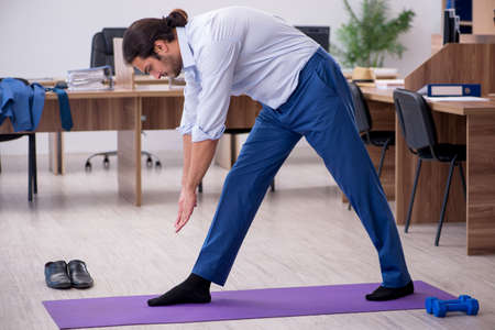 Young male employee doing sport exercises during breakの写真素材