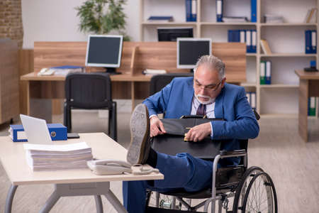 Old businessman employee in wheel-chair working in the officeの写真素材