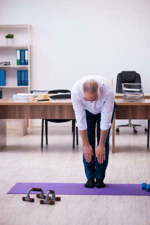Old businessman employee doing sport exercises in the officeの写真素材