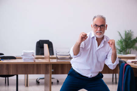 Old businessman employee doing sport exercises in the officeの写真素材