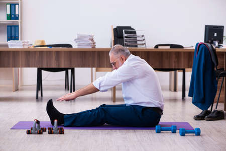Old businessman employee doing sport exercises in the officeの写真素材