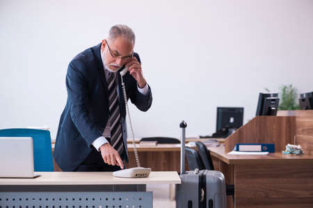 Old male employee preparing for travel in the officeの写真素材