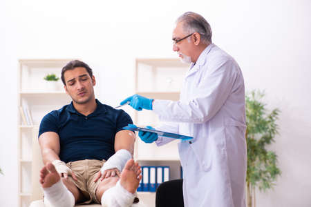 Young injured man visiting old doctor traumatologistの写真素材