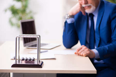Old male employee businessman and meditation balls on the deskの写真素材