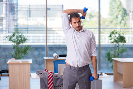 Young male employee doing sport exercises in the officeの写真素材
