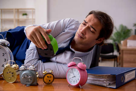 Young male employee sleeping in the office in time management coの写真素材