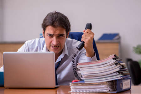 Young male employee unhappy with excessive work in the officeの写真素材