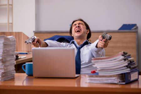 Young male employee unhappy with excessive work in the officeの写真素材