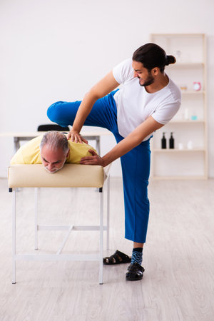 Old male patient visiting young male doctor chiropractorの写真素材