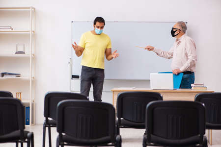 Young male student and experienced teacher in pandemic conceptの写真素材