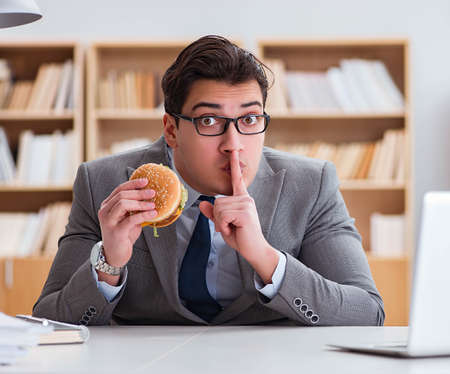 Hungry funny businessman eating junk food sandwichの写真素材
