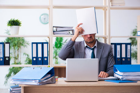 Young male employee and too much work in the officeの写真素材