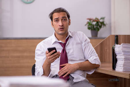 Young male employee drinking alcohol in the officeの写真素材