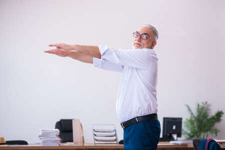 Old businessman employee doing sport exercises in the officeの写真素材