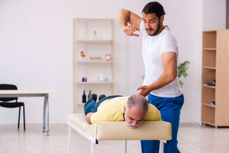 Old male patient visiting young male doctor chiropractorの写真素材