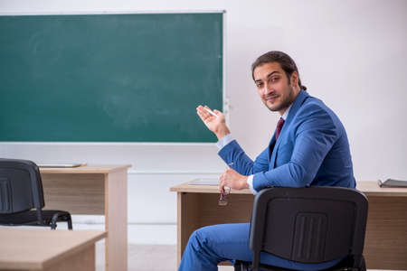 Young male teacher in suit in front of green boardの写真素材