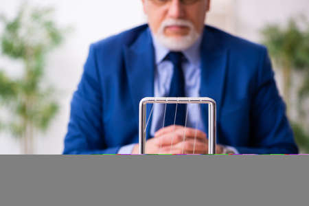 Old male employee businessman and meditation balls on the deskの写真素材