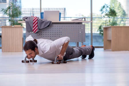 Young male employee doing sport exercises in the officeの写真素材