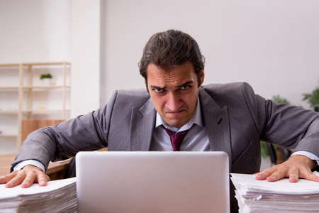Young male employee unhappy with excessive work in the officeの写真素材