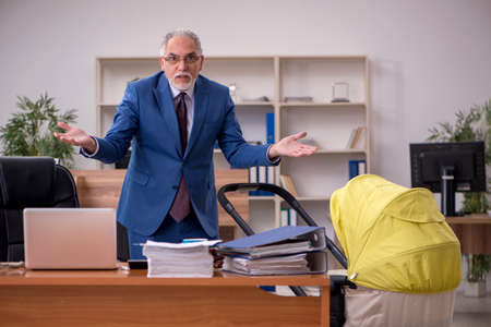 Aged businessman employee looking after newborn at workplaceの写真素材