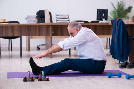 Old businessman employee doing sport exercises in the office