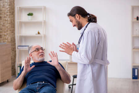 Old male patient visiting young male doctor chiropractorの写真素材