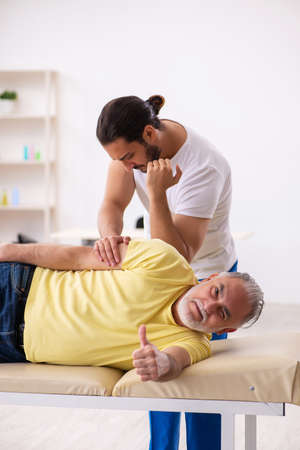 Old male patient visiting young male doctor chiropractorの写真素材