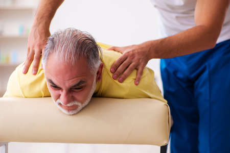 Old male patient visiting young male doctor chiropractorの写真素材