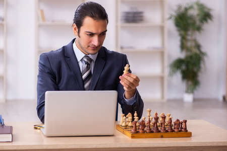 Young male employee playing chess at workplaceの写真素材