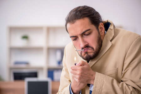 Ill cigarette addicted male employee working in the officeの写真素材