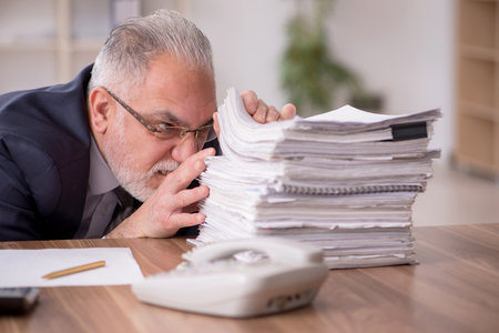 Aged male employee unhappy with excessive work in the officeの写真素材