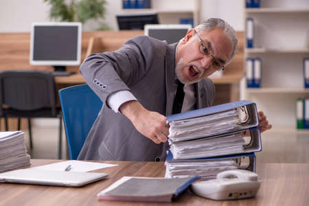 Old male employee unhappy with excessive work in the officeの写真素材