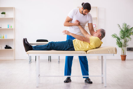 Old male patient visiting young male doctor chiropractorの写真素材