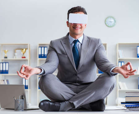 Businessman in virtual reality VR glasses meditating at desk topの写真素材