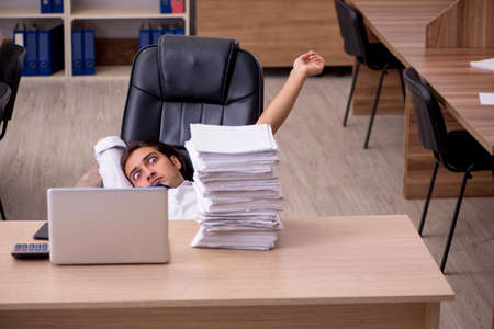 Young male employee unhappy with excessive work in the officeの写真素材