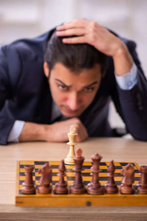 Young male employee playing chess at workplaceの写真素材