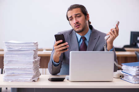 Young male employee unhappy with excessive work in the officeの写真素材