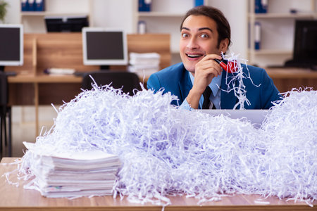 Young male employee and a lot of cut papers in the officeの写真素材