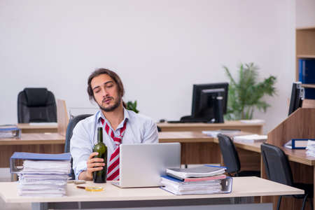 Young male employee drinking alcohol in the officeの写真素材
