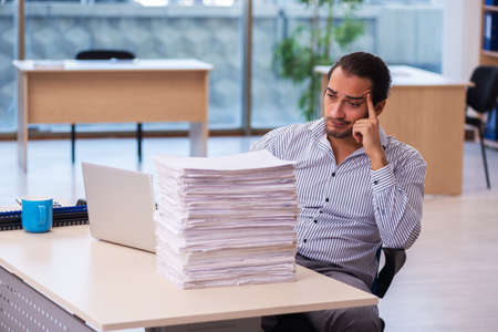 Young male employee unhappy with excessive work in the officeの写真素材