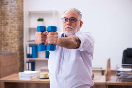 Old businessman employee doing sport exercises in the officeの写真素材