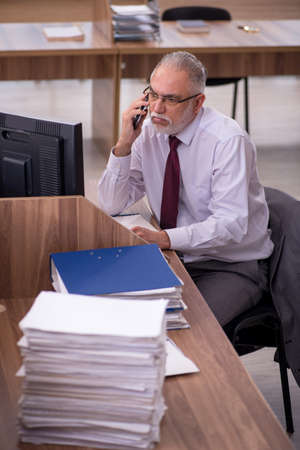 Old businessman employee and too much work in the officeの写真素材