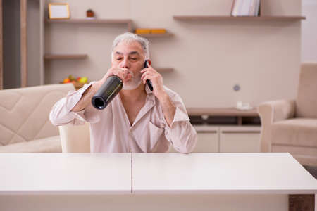Old man drinking alcohol at homeの写真素材