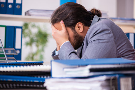Young male employee unhappy with excessive work in the officeの写真素材