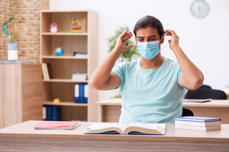 Young male student sitting in the classroom wearing maskの写真素材