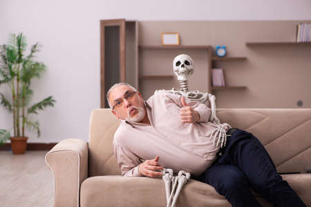 Old man sitting on the sofa with the female skeletonの写真素材