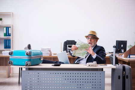 Old male employee preparing for travel in the officeの写真素材