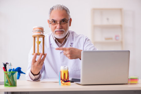 Old male dentist in time management conceptの写真素材