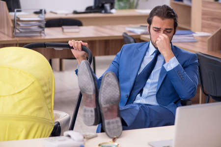 Young male employee looking after new born at workplaceの写真素材
